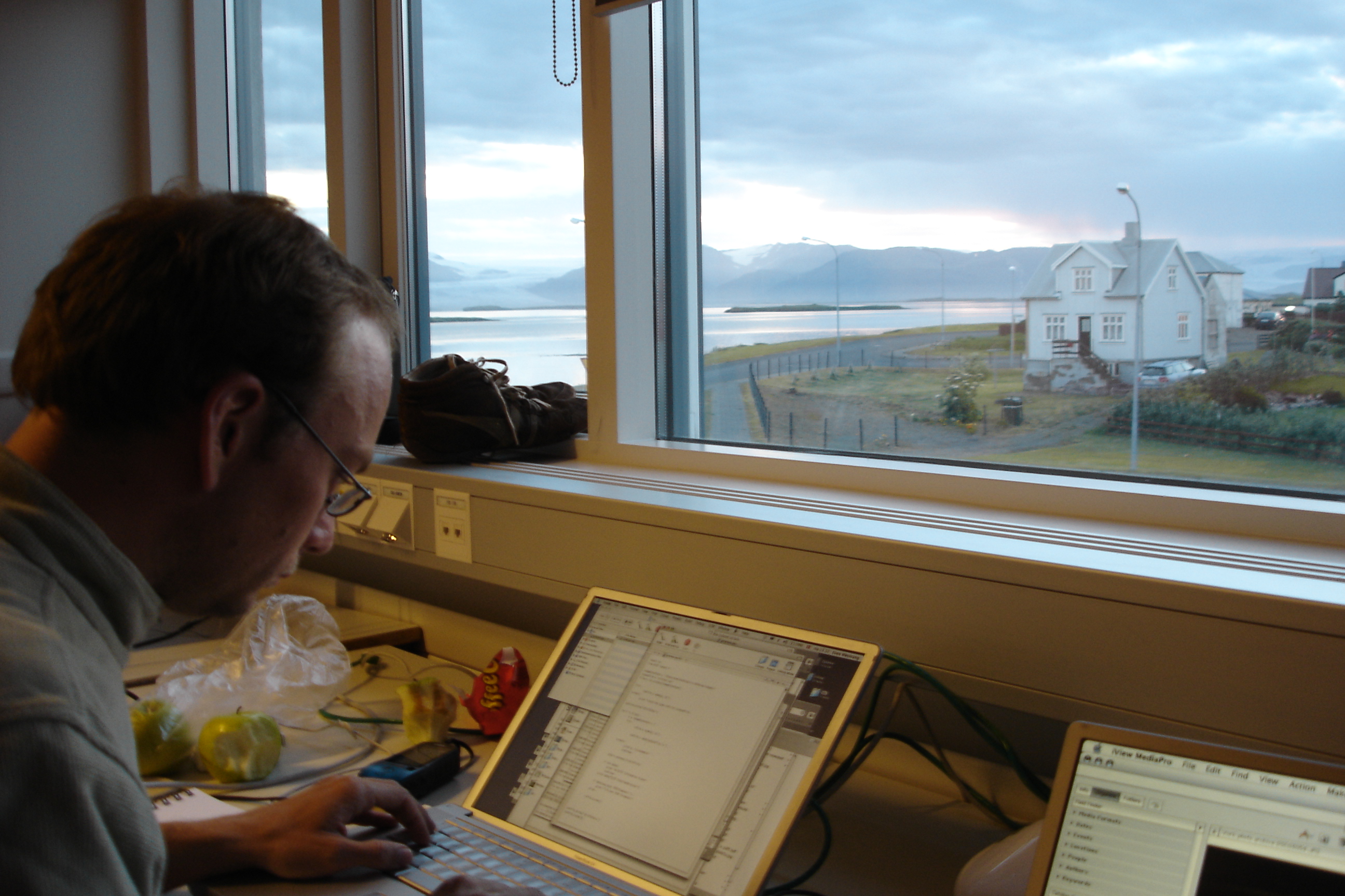 Even Westvang at his laptop in the workshop, head down, typing. Through the windows: the fjord at dawn, mist over the water, a white Icelandic house on the road outside.